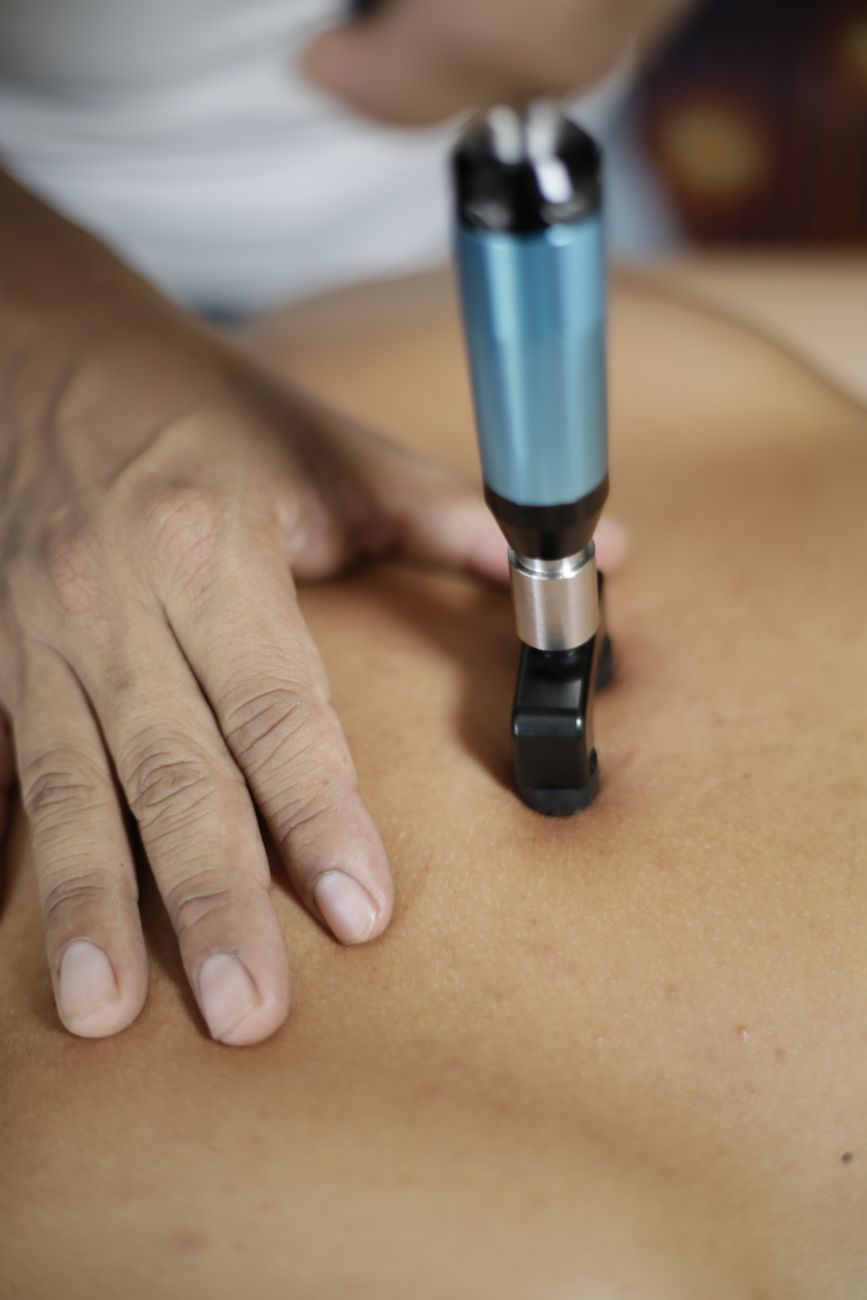 A shockwave therapy applicator in use, steadied by a practitioner's hand